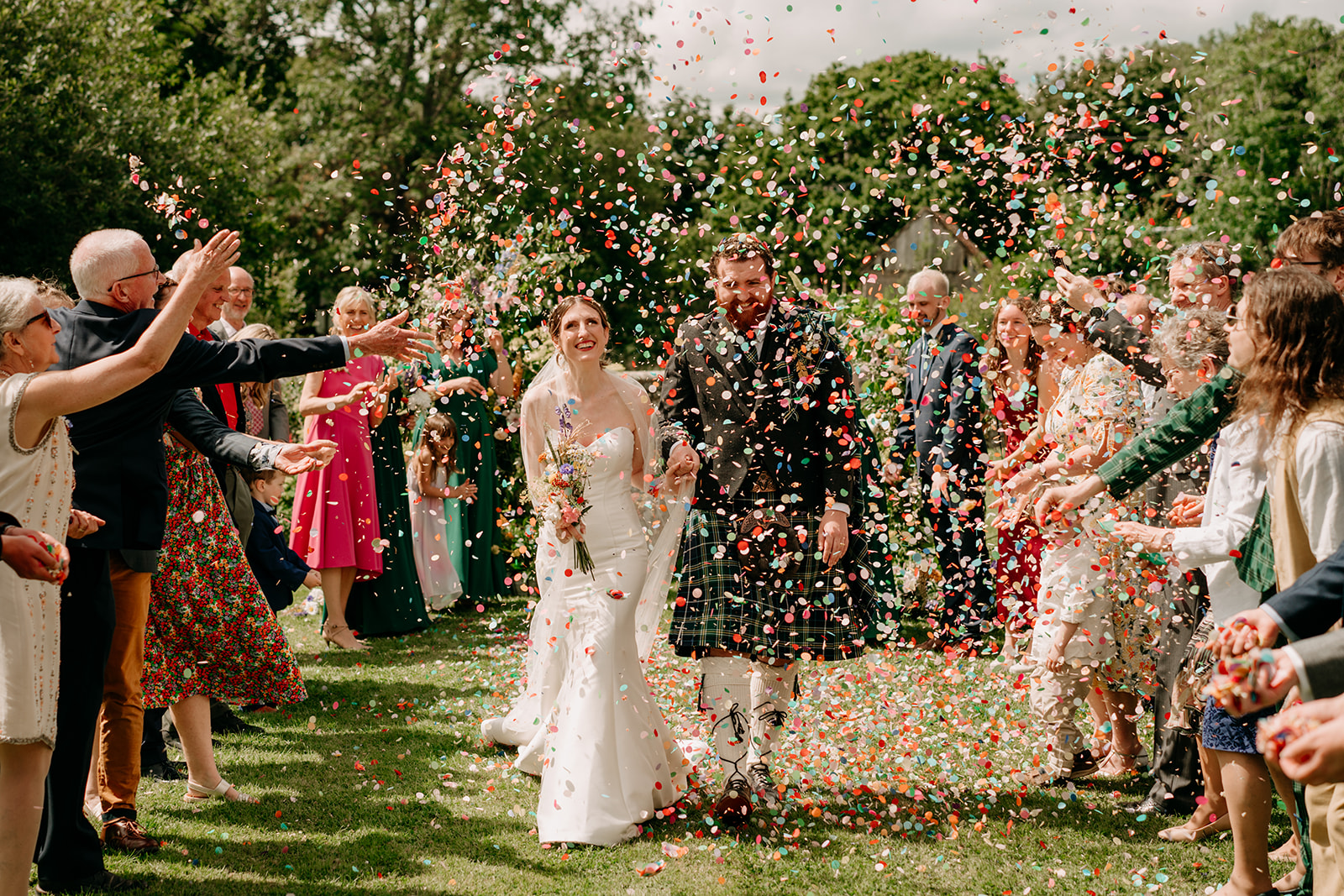 Bride and groom walking down the wedding aisle with guests throwing colourful confetti in front of them